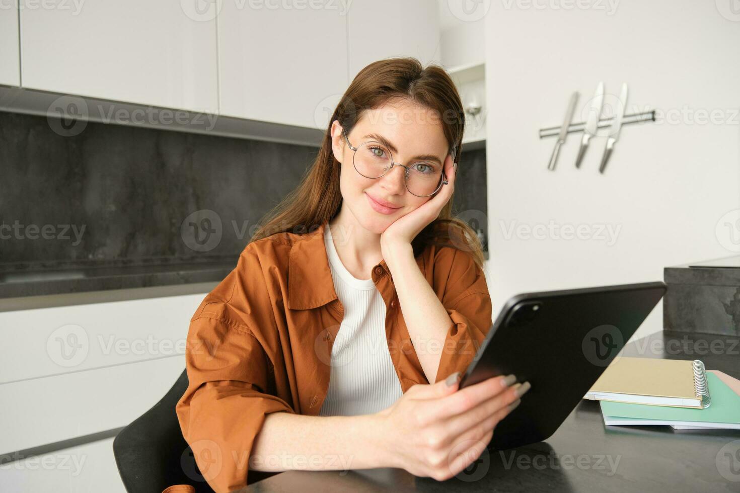 Portrait of cute woman, student in glasses, sitting in kitchen with digital tablet, working remotely, making home as workplace, teacher giving lessons online photo