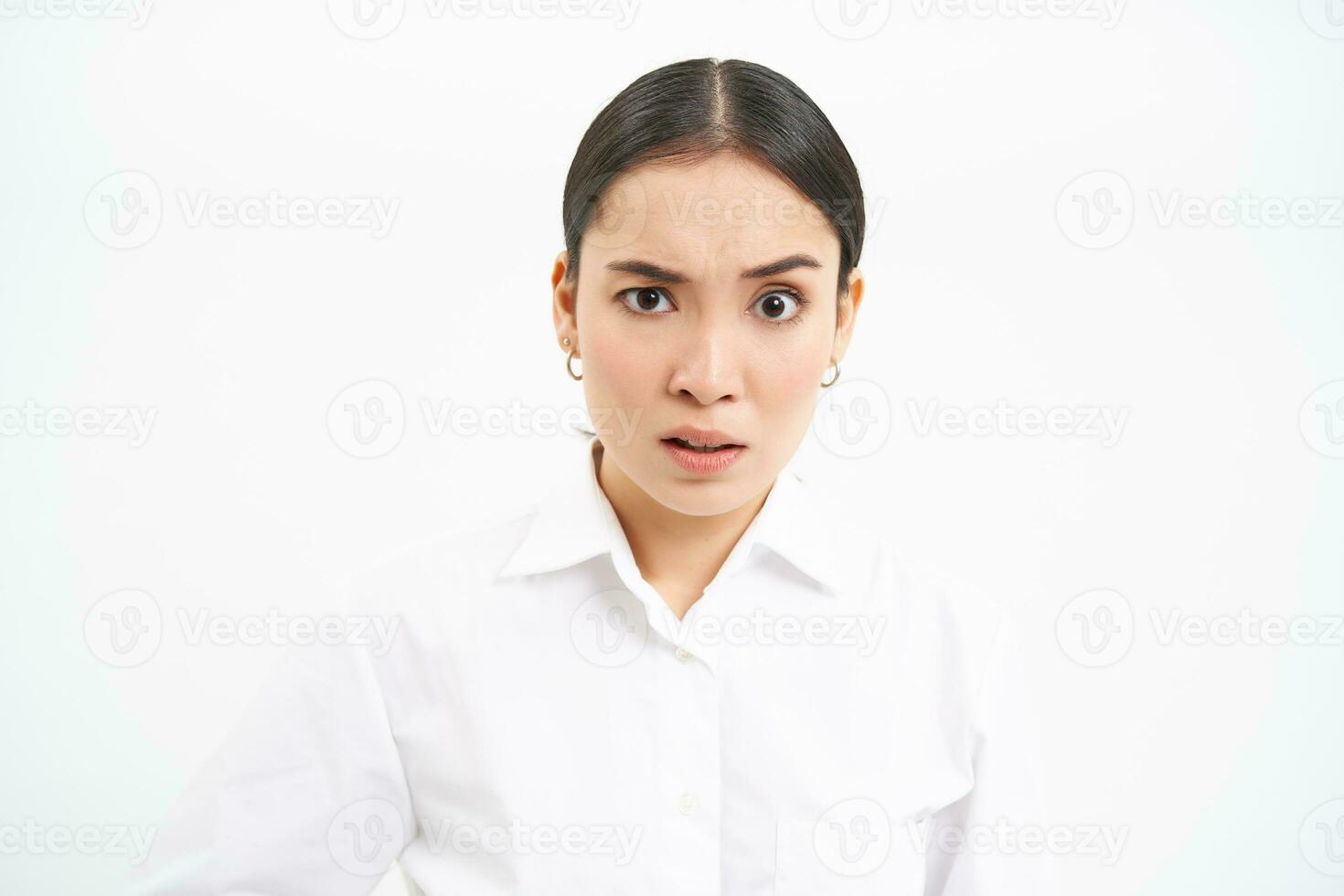 Portrait of asian businesswoman, office lady with shocked face, looks confused at camera, stands over white background photo