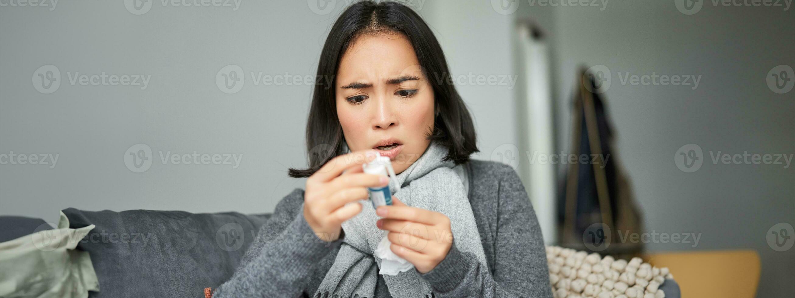 Ill korean woman looking at thermometer with concerned face, catching cold, having fever, having covid, staying at home on sick leave photo