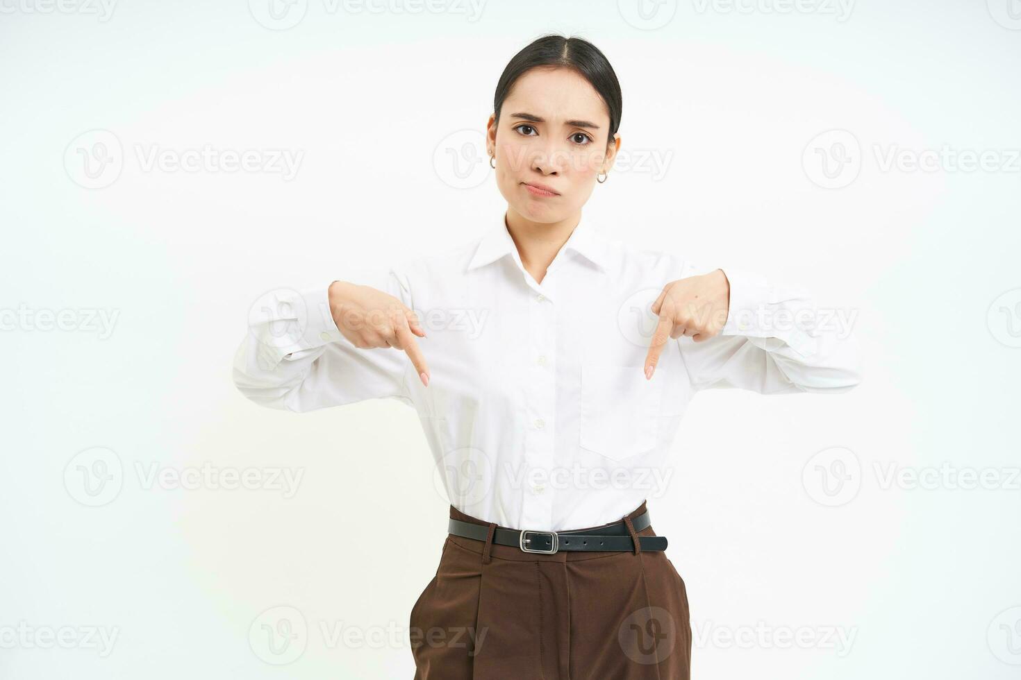 Disappointed lady boss, young woman points down with concerned, frowning face expression, white background photo
