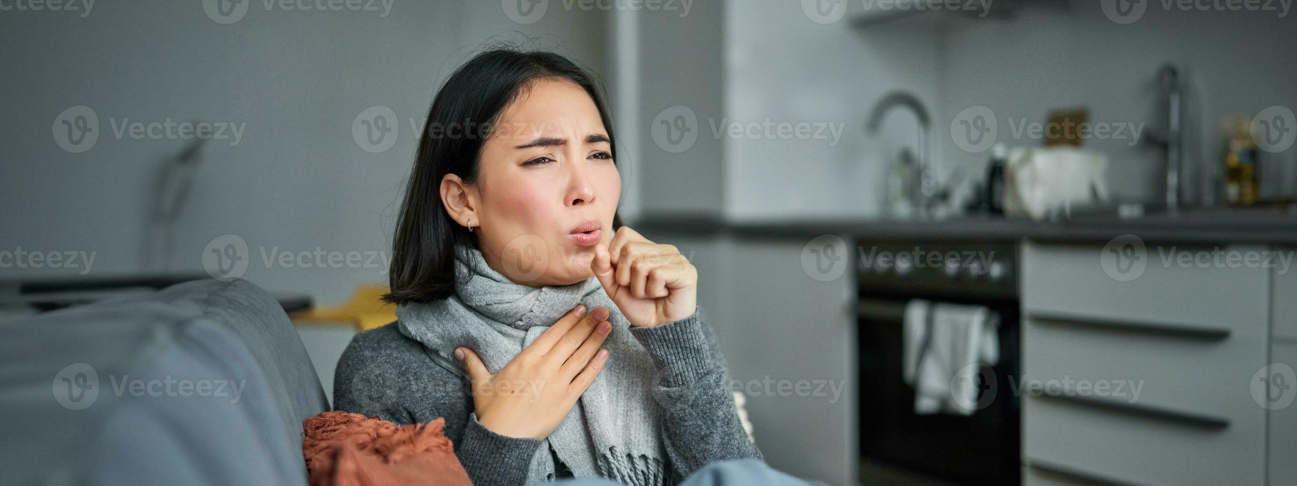Sick korean woman coughing and feeling unwell, grimacing, has influenza, cought cold or flu, staying at home photo