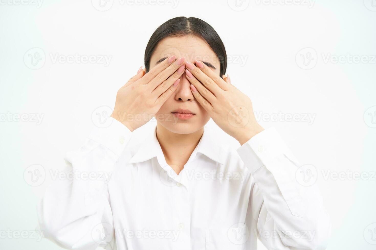 Asian woman entrepreneur, businesswoman shuts her eyes with hands, stands blindfolded against white studio background photo