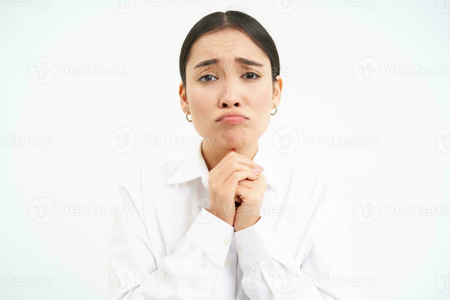 Upset young saleswoman, asian woman holds hands in pray, begs you, asks for favour with sad face, pleading, standing over white background photo