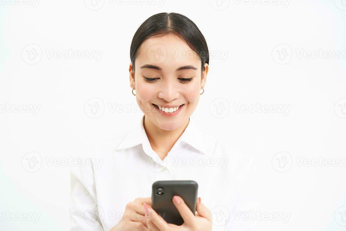 Business and corporate people. Young asian female entrepreneur, looking at smartphone, working on mobile phone, standing over white background photo