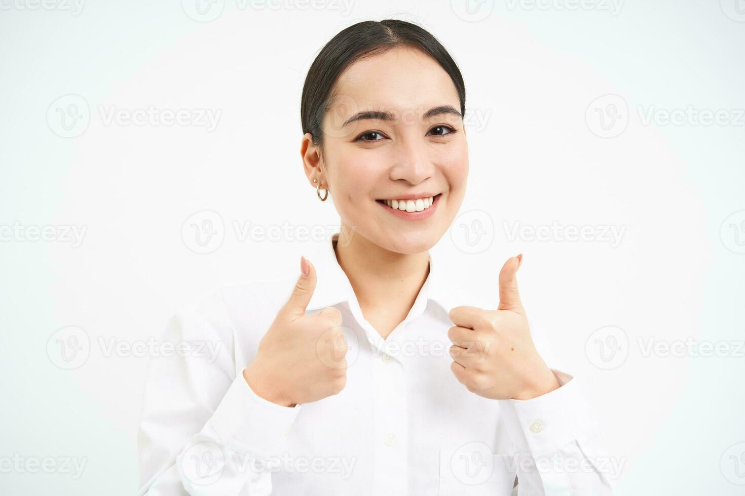 Portrait of asian businesswoman shows thumbs up, approves smth, recommends company, stands over white background photo