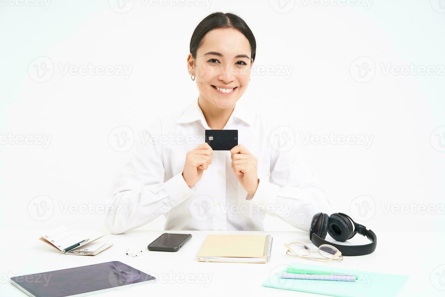 Happy businesswoman sits in office, shows credit card and smiles, pays contactless, waiting for payday, white background photo
