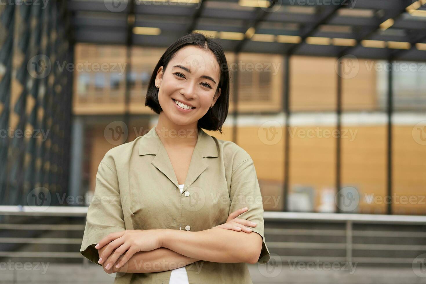 Portrait of young asian woman standing with confidence, cross arms on chest and smiling, posing outdoors on street photo