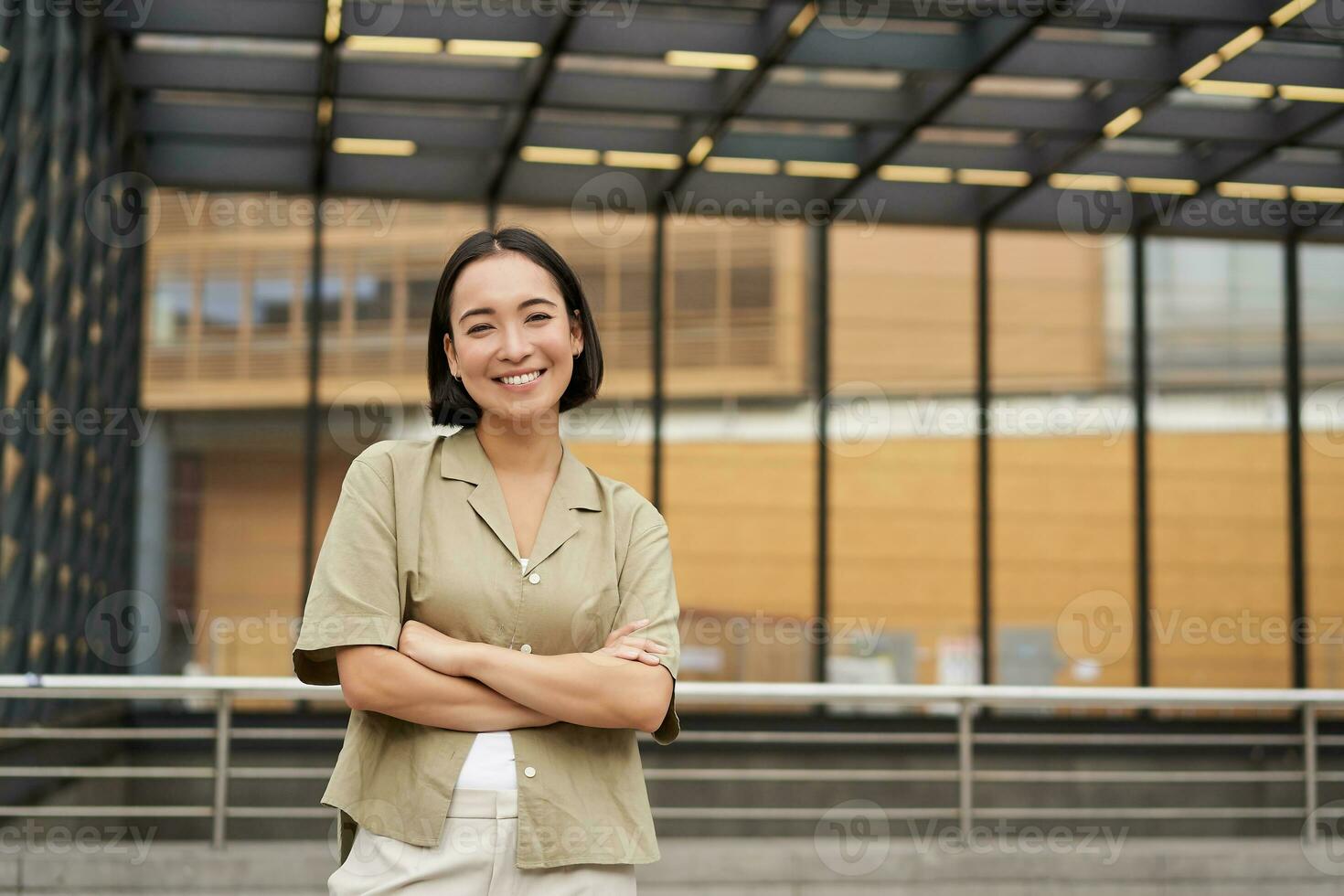 Portrait of young asian woman standing with confidence, cross arms on chest and smiling, posing outdoors on street photo