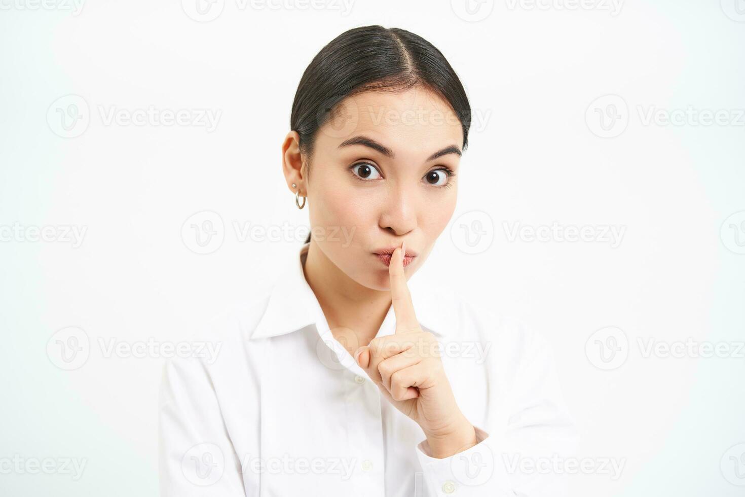 Office gossips. Young woman shushing, press finger to lips, say shh, tells secret, asks to keep quiet, stands over white background photo