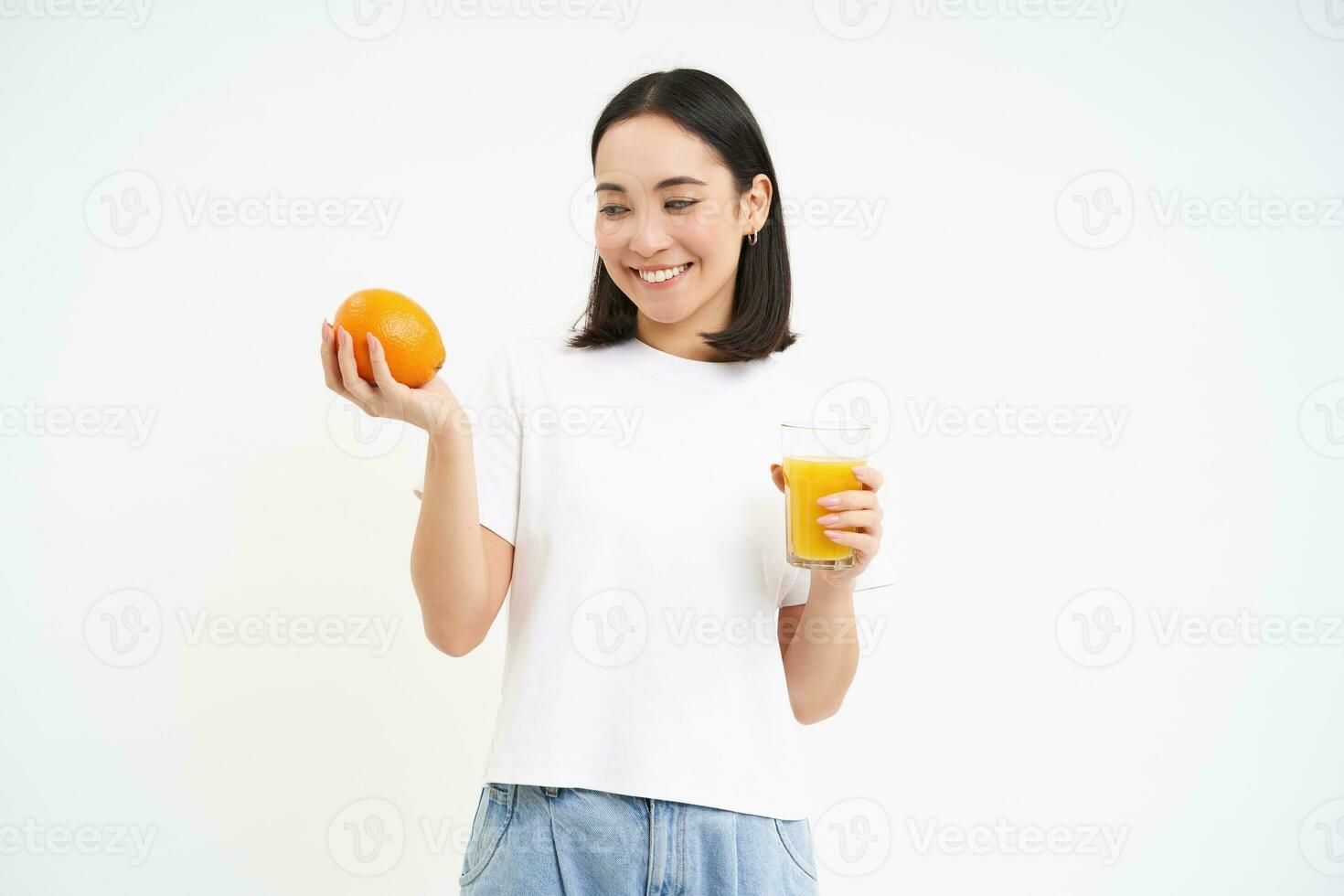 Beautiful and healthy young woman, starts her day with fresh juice, holding orange fruit and smiling, white background photo