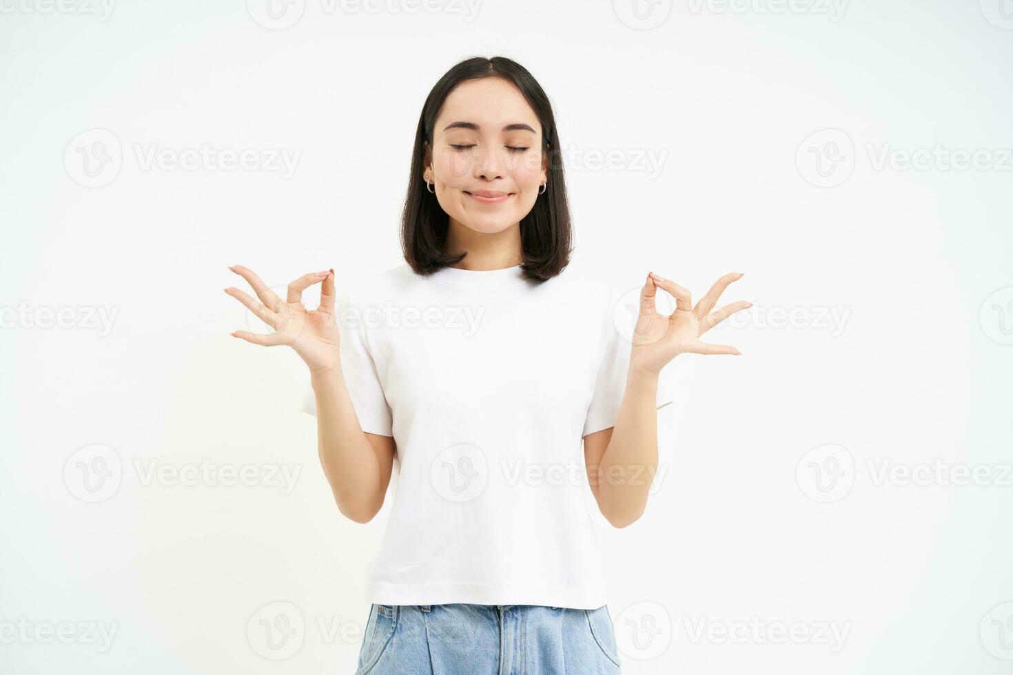 Peaceful smiling asian woman, standing calm and relaxed, holds hands in zen, meditation pose, isolated over white background photo