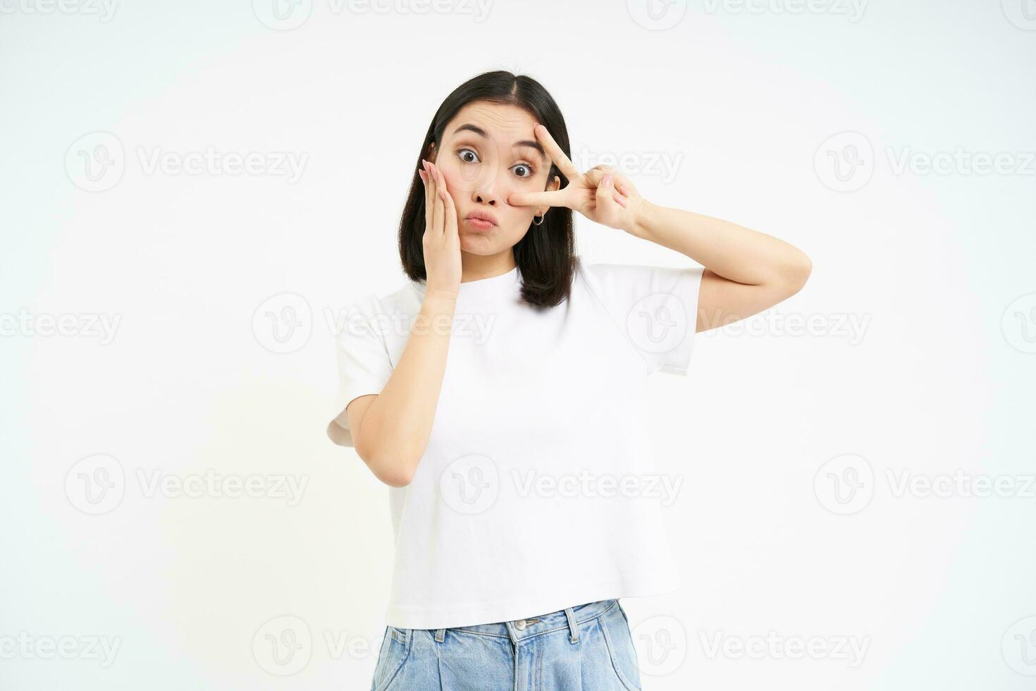 Positive korean girl, shows peace, v-sign and kissing face, posing cute against white background photo