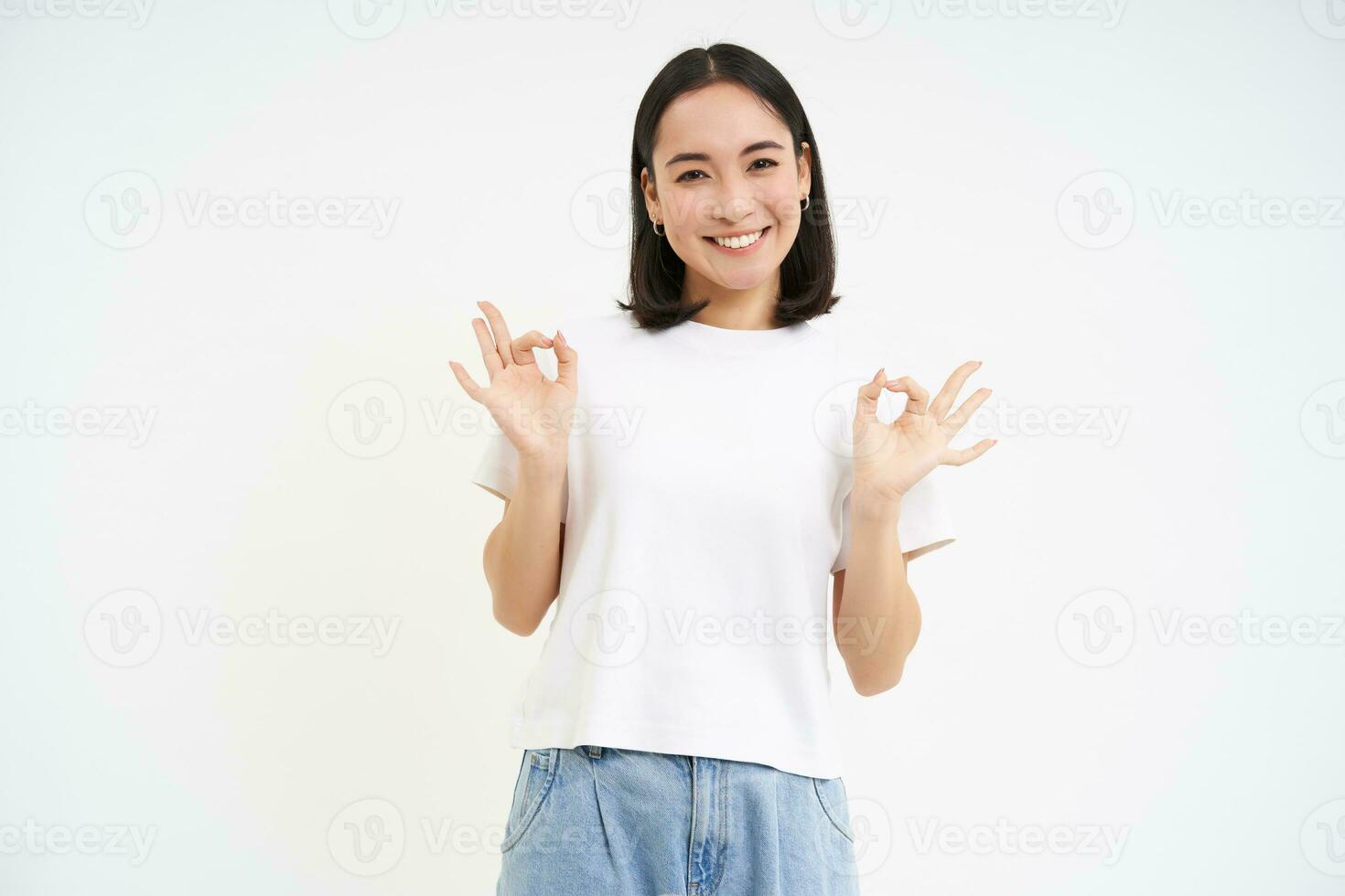 Image of asian woman, shows okay, ok sign in approval, recommends product, gives positive feedback, white studio background photo