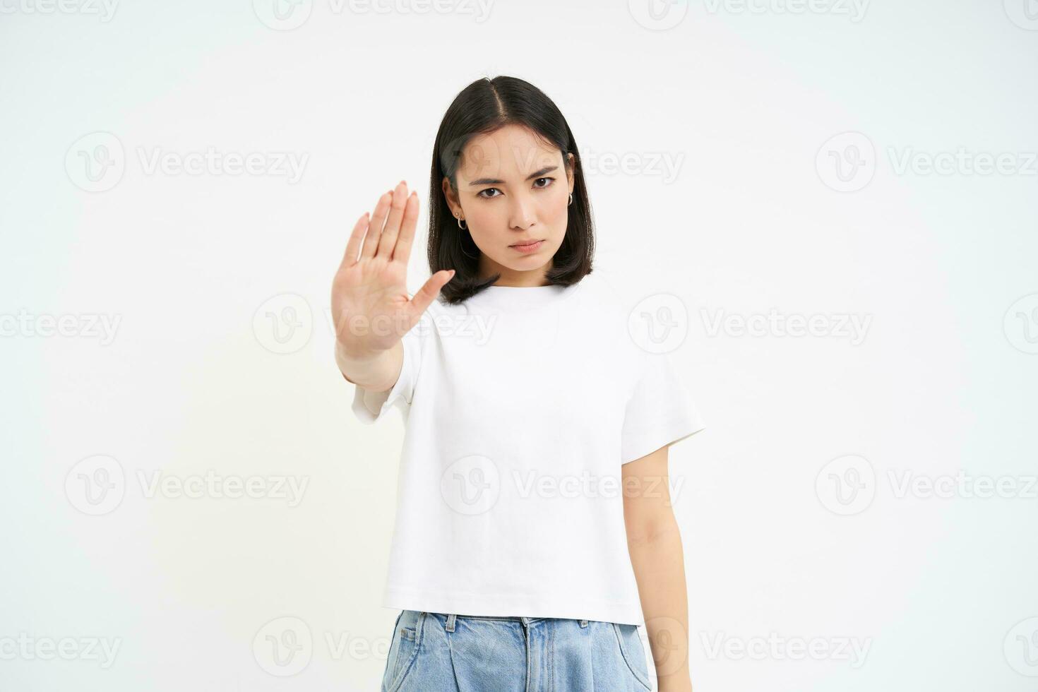 Young serious woman shows stop sign, rejects smth, disapprove and ban action, stands over white background photo