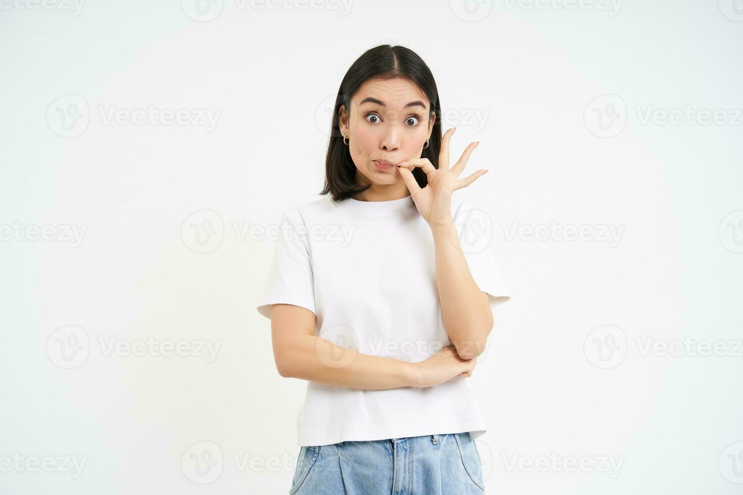 Asian woman hears gossips and zips her mouth, seal lips to keep promise, stands over white background photo