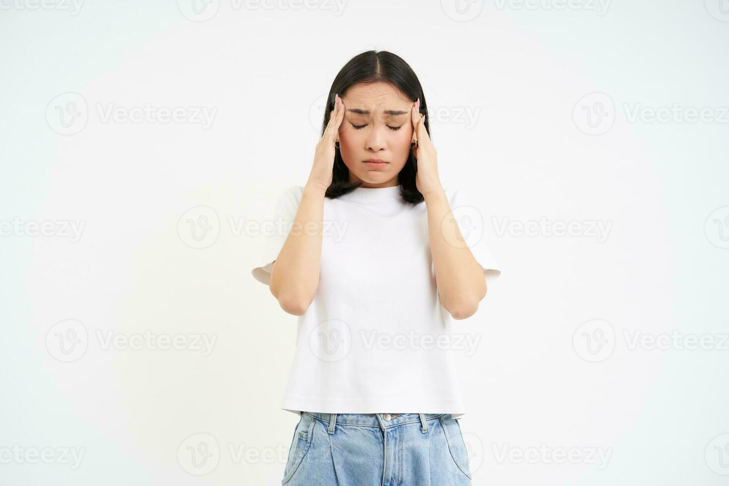 Sad woman holds hands on head, suffers headache, has migraine, feels dizzy, stands over white background photo