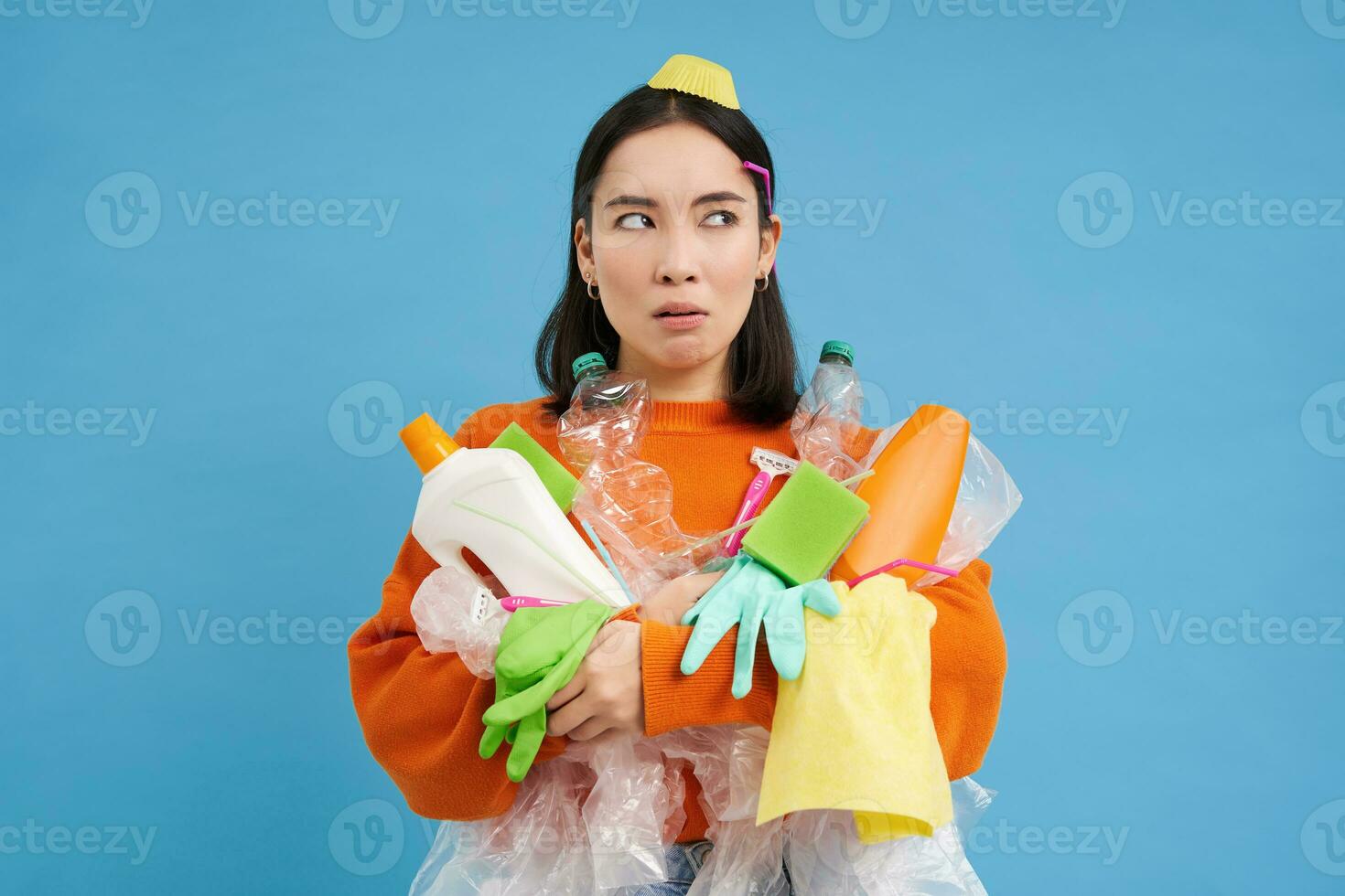 Portrait of asian woman thinking, holding empty plastic bottles, recycable waste, sorting litter to recycle, blue background photo