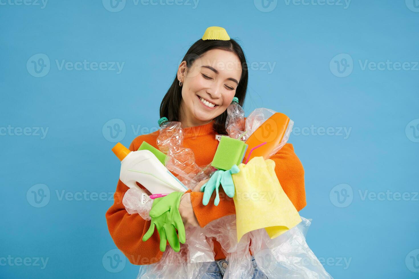 Portrait of smiling asian woman hugging empty plastic bottles and recycable garbage, eco-activist likes to recycle, blue background photo