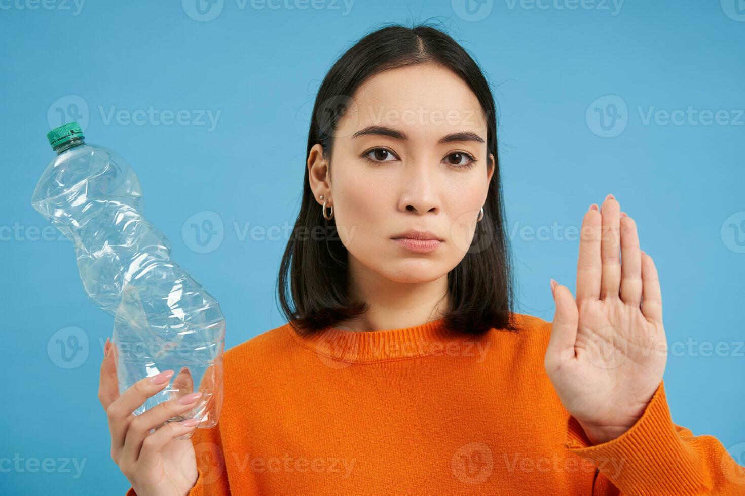 Serious asian woman tells to recycle, shows plastic bottle and urges sort and collect waste to recycling centers, blue background photo