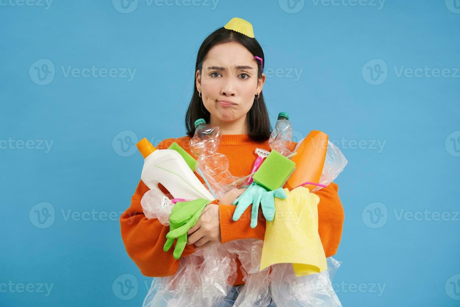 Complicated girl with garbage on her face, plastic empty bottles and waste, looking troubled and sad, blue background photo