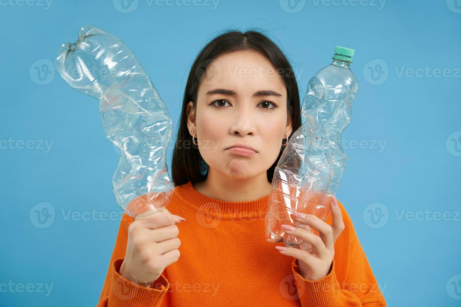 Thinking angry girl, shows two bottles, recycling plastic, goes green, reusable trash, blue background photo