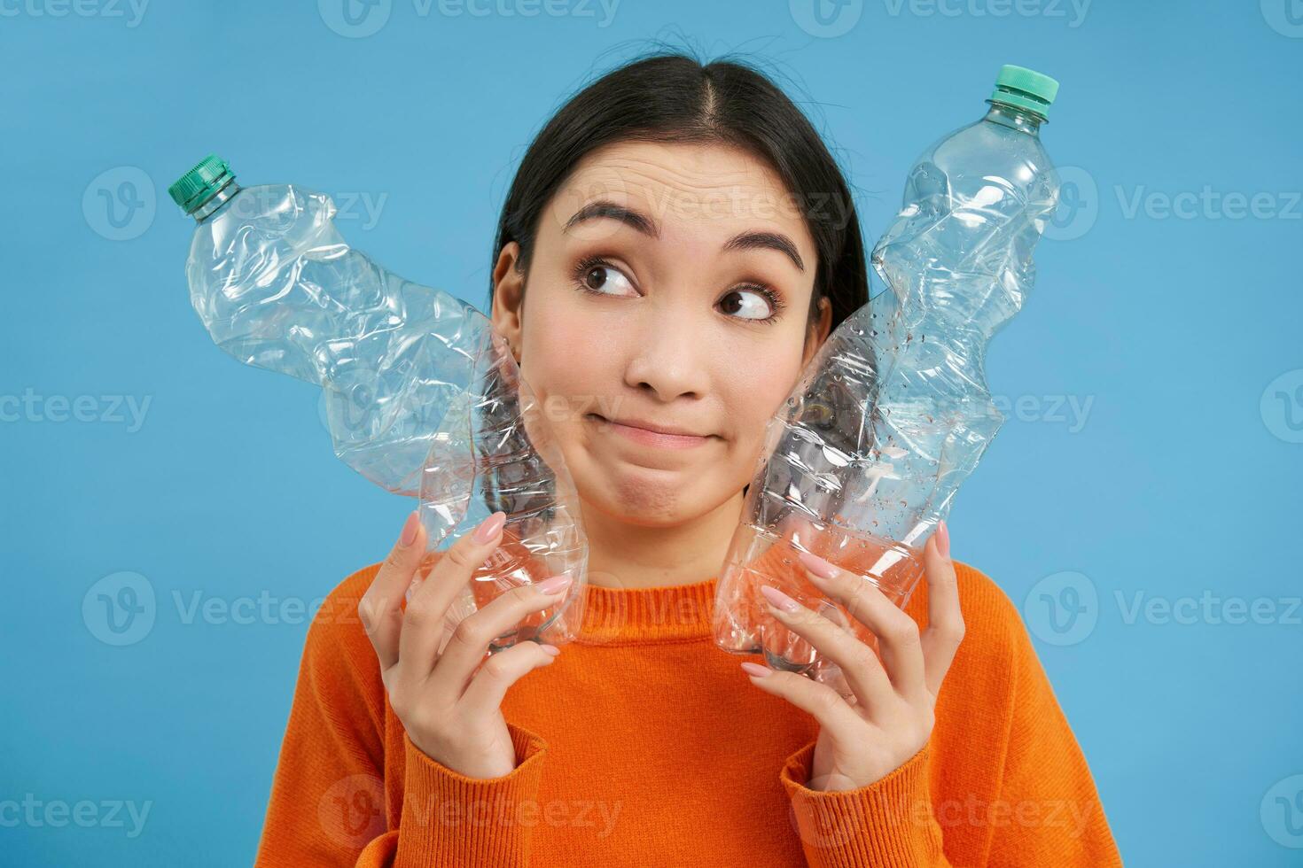 Thoughtful korean woman shows two plastic bottles, looks clueless and puzzled, concept of recycling and ecology photo