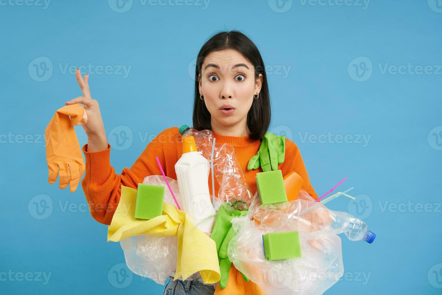 Asian woman looks shocked, holds plastic rubbish, sorting garbage for recycling, looks surprised, blue background photo