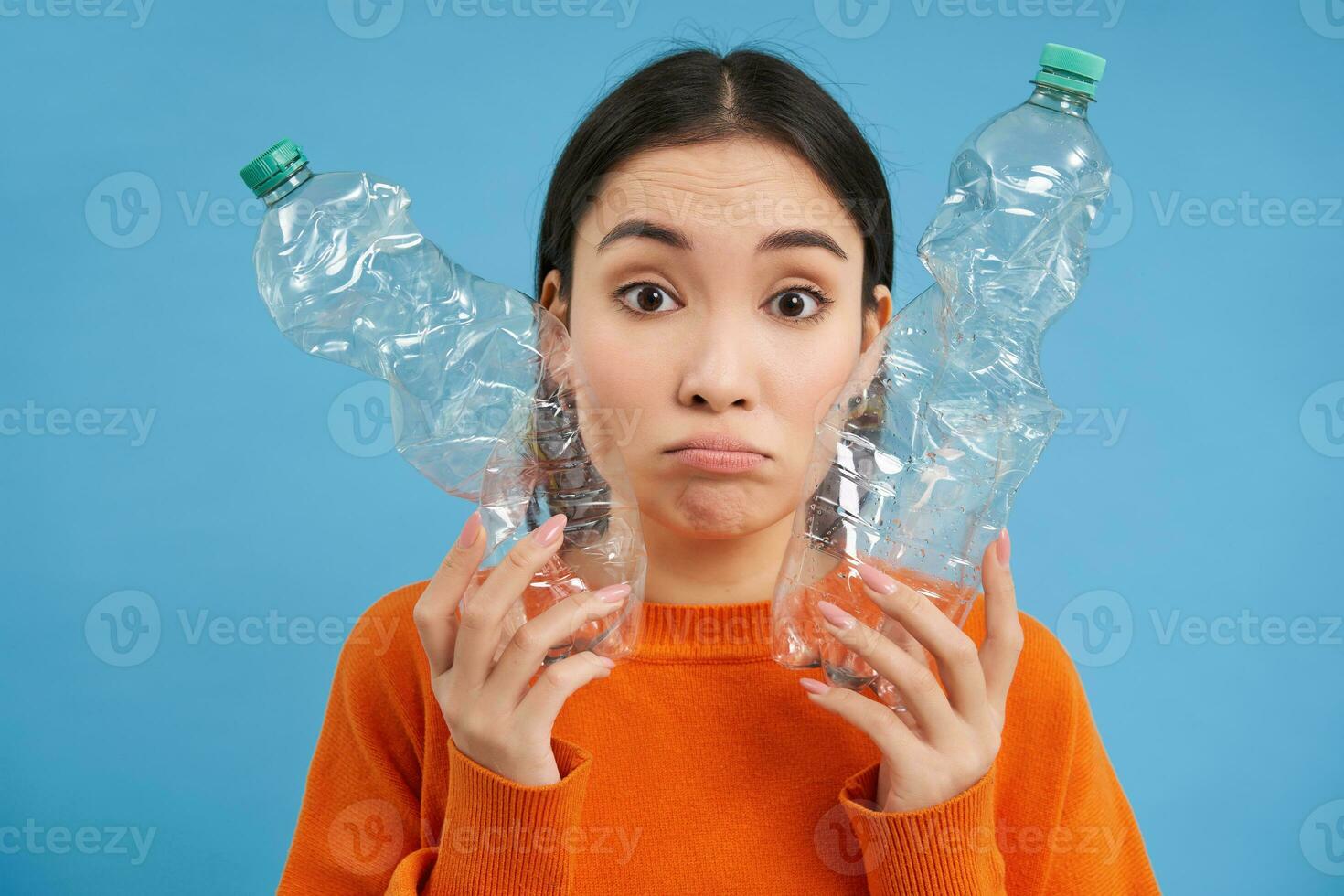 Portrait of sad asian woman with plastic bottles, upset by lack of recycling centers, blue background photo