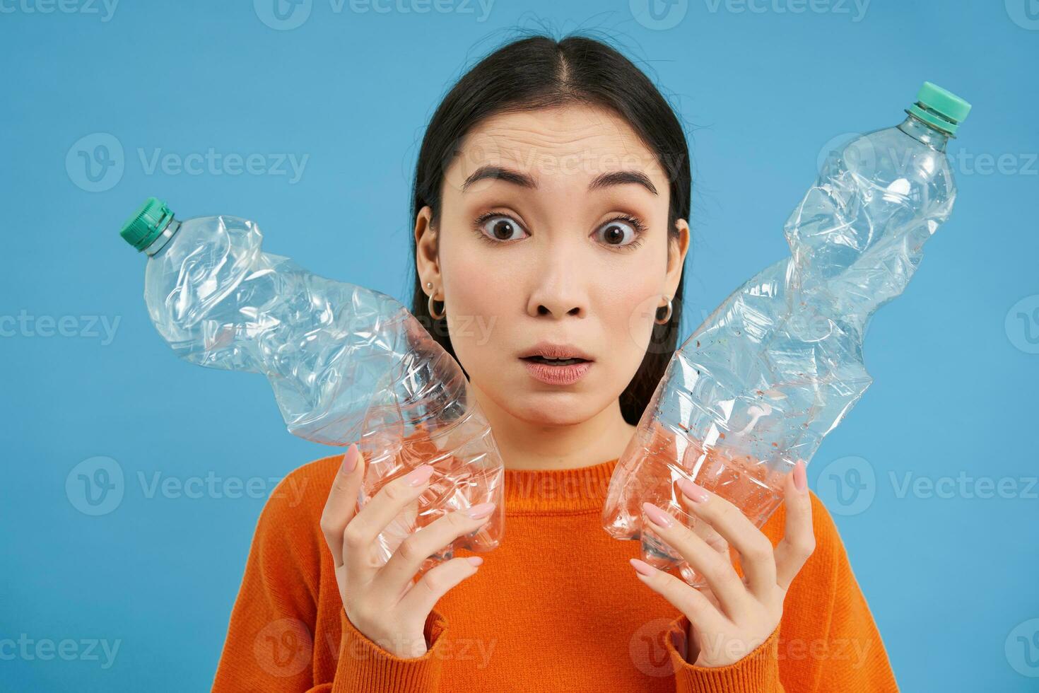 Portrait of girl with two plastic bottles, looks confused, tried to recycle, sorting garbage, isolated on blue background photo