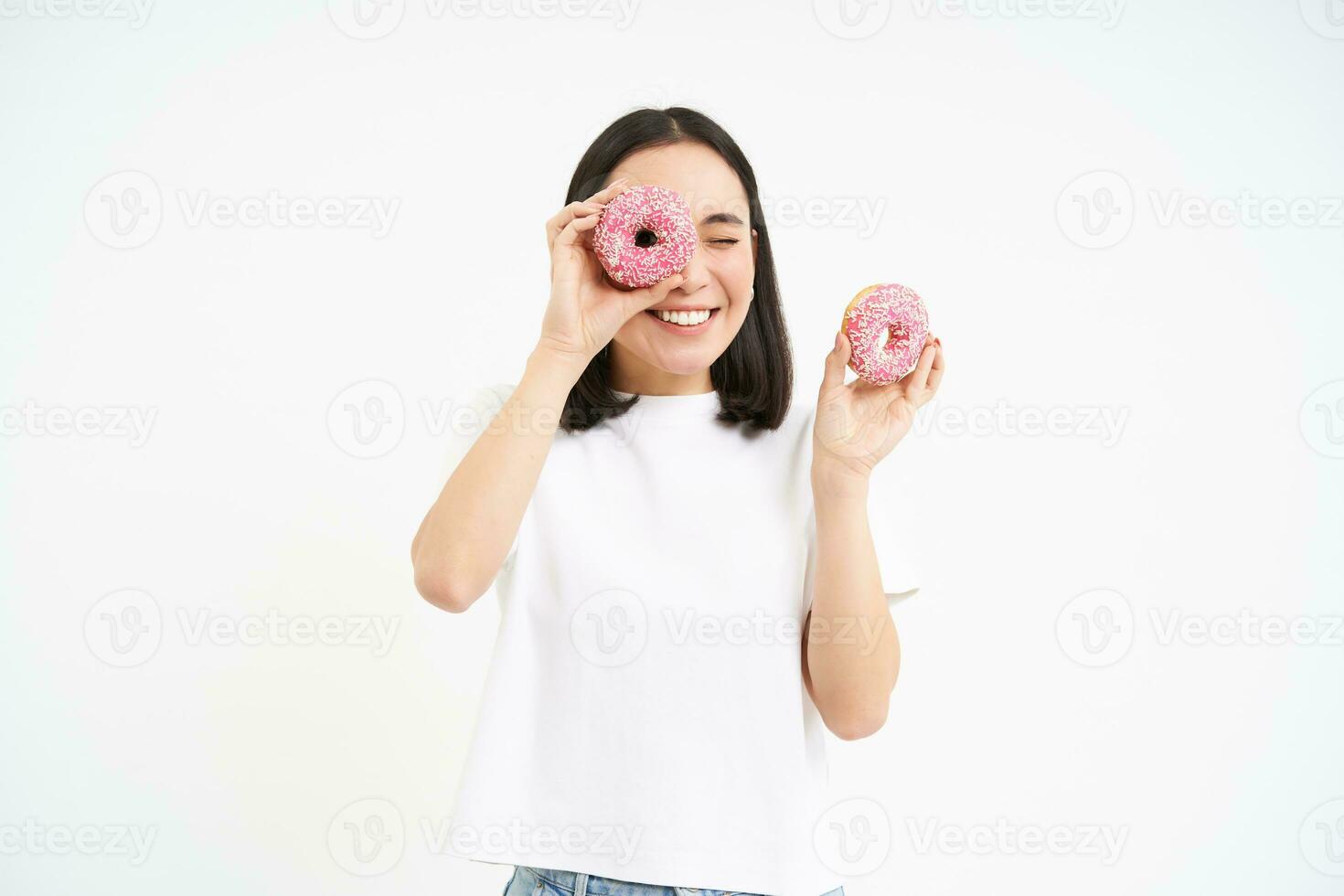 retrato de contento coreano mujer, hace lentes desde dos sabroso vidriado donas, sonriente y teniendo divertido, blanco antecedentes foto