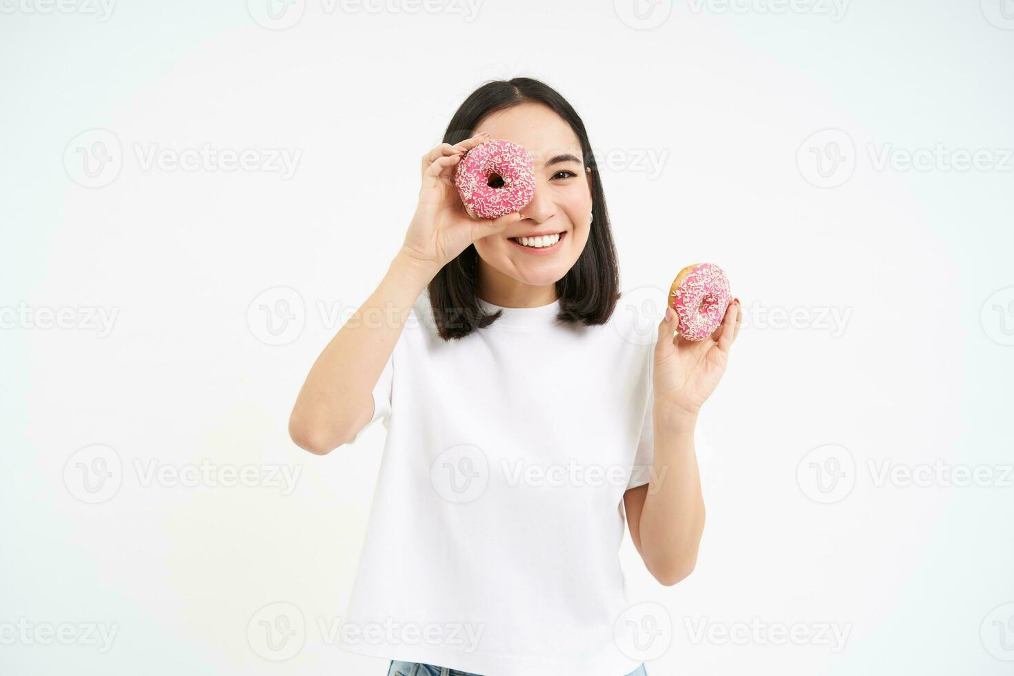 Cute smiling korean woman, looks through doughnut holes, eating tasty donnuts, isolated over white background photo