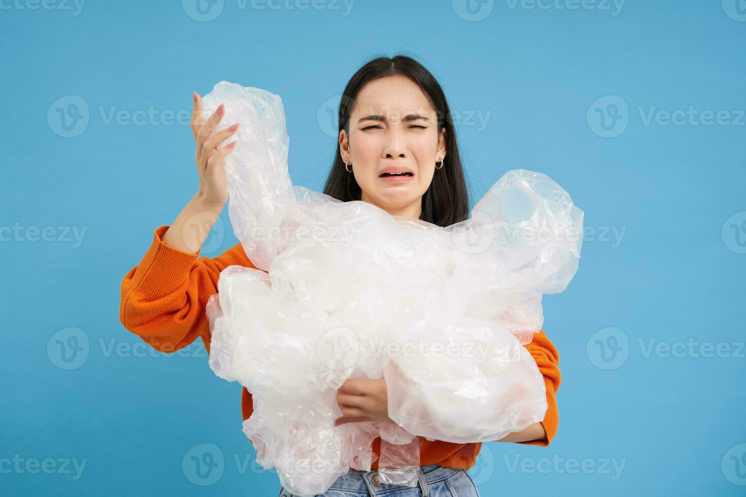 Crying asian woman with plastic recycling waste, tired of sorting garbage into different bins, preserving nature, blue background photo