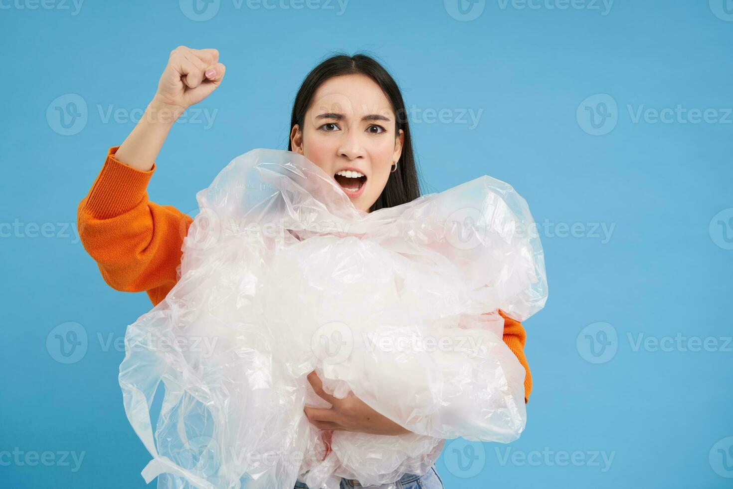 Angry eco-activist holding plastic waste, raising fist and fighting for environment, sorting garbage, recycling, blue background photo