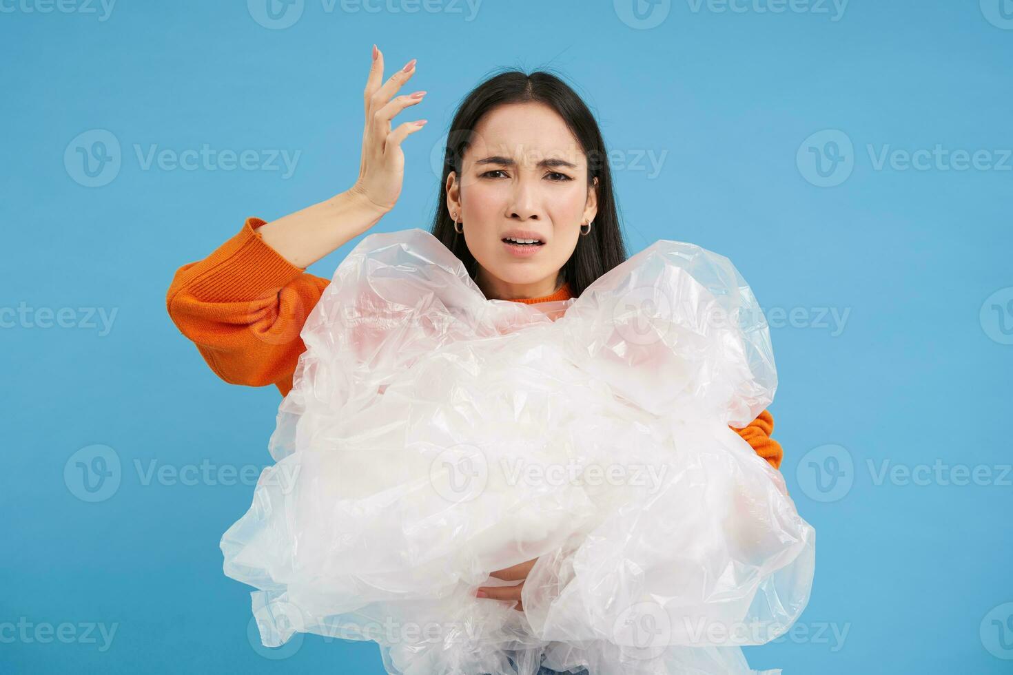 Annoyed asian woman volunteer, holding plastic waste, shouting with disappointed face, hates polution, stands over blue background photo