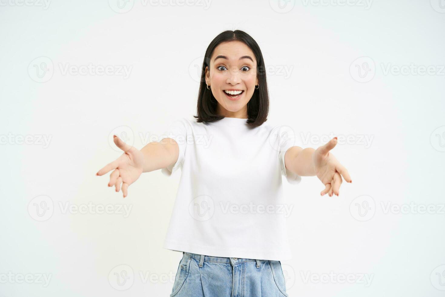 Friendly smiling asian woman, reaching her hands towards camera, hugging, welcoming you, standing over white background photo