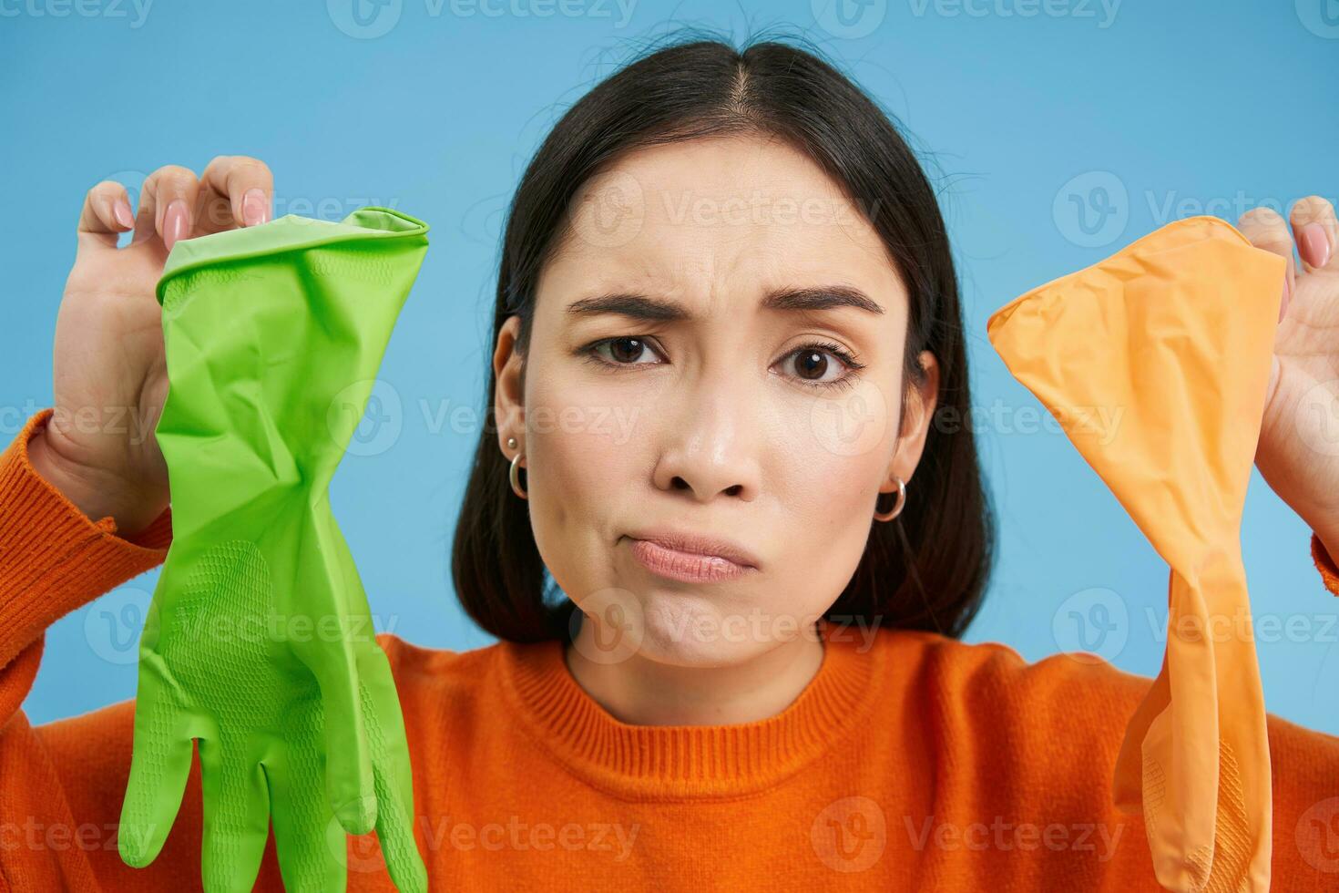 Close up of upset woman showing two dirty used gloves, frowning upset, dislikes cleaning house, blue background photo