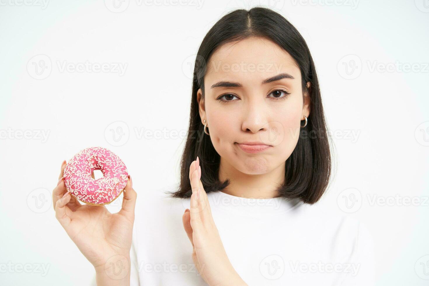 No sweets. Serious young woman on diet, showing stop gesture and glazed doughnut, disapprove junk food, white background photo