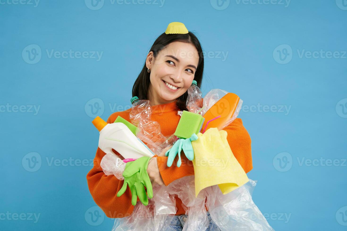 Portrait of smiling asian woman hugging empty plastic bottles and recycable garbage, eco-activist likes to recycle, blue background photo