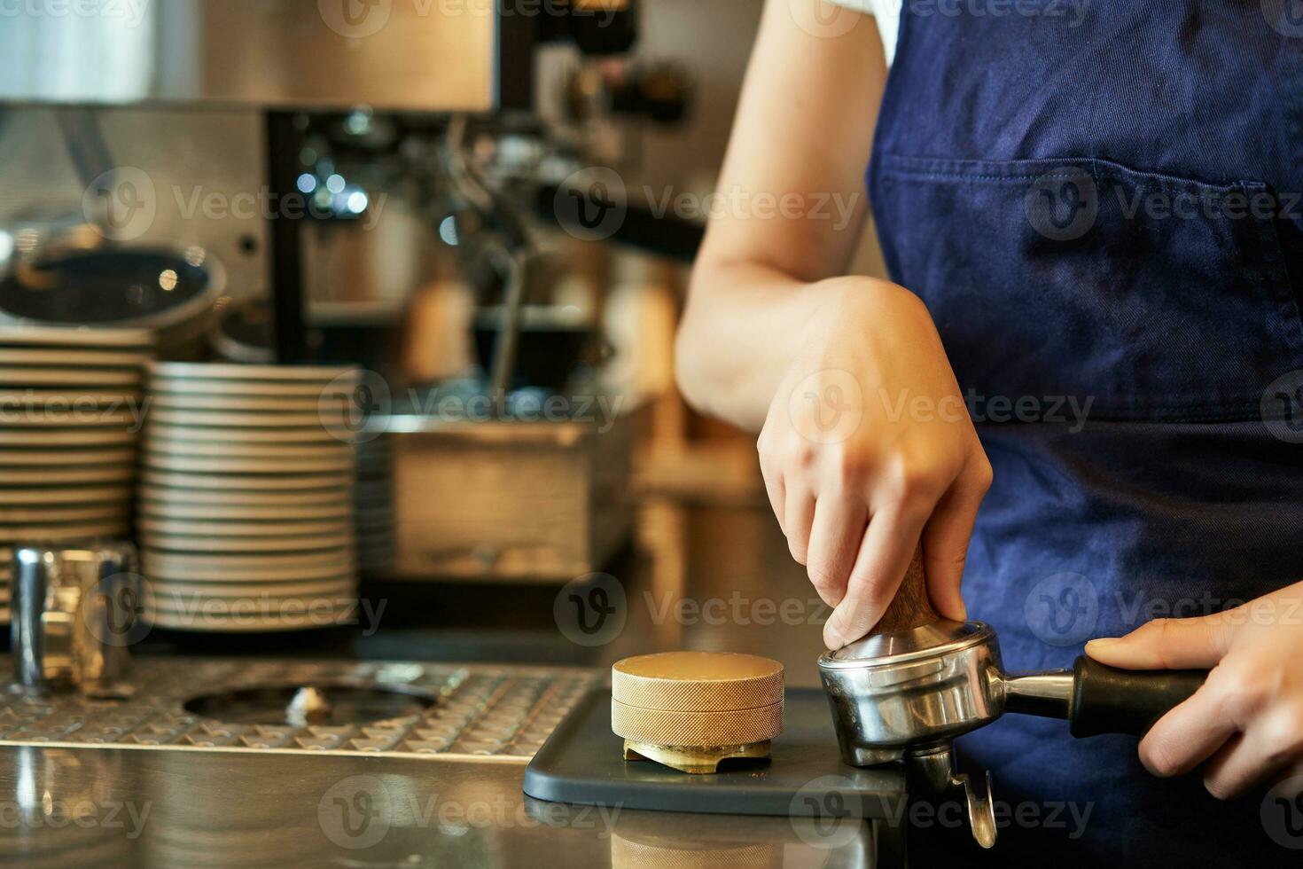 Close up of barista female hands pressing coffee into tamper, prepares order in cafe behind counter photo