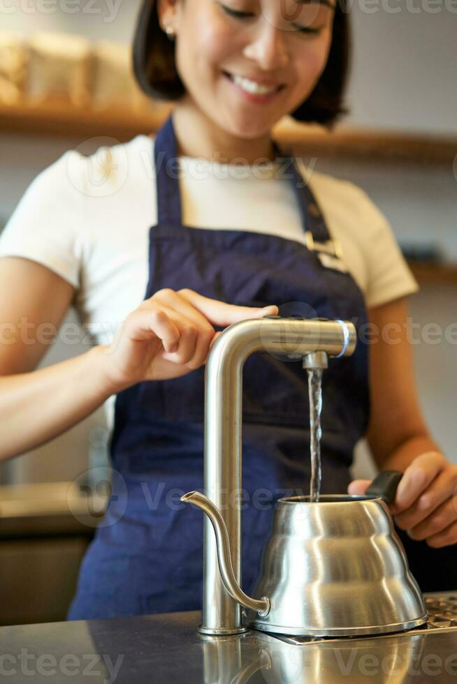 Vertical shot of girl barista in cafe pouring water from tap, using kettle to brew filter coffee photo