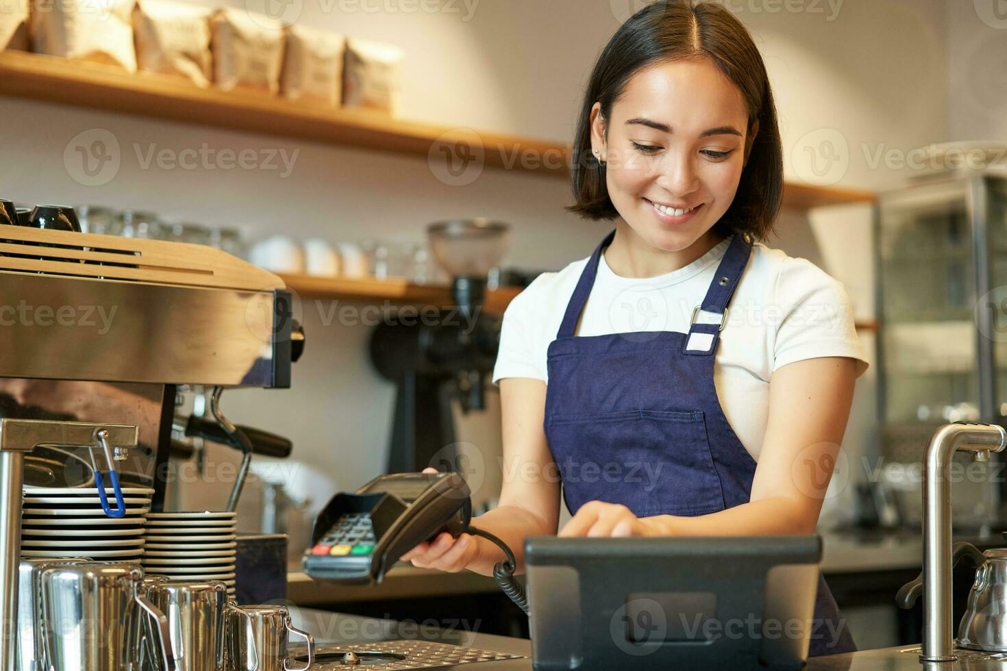 Smiling asian barista girl processing order, enter order in POS terminal, working at counter in coffee shop photo