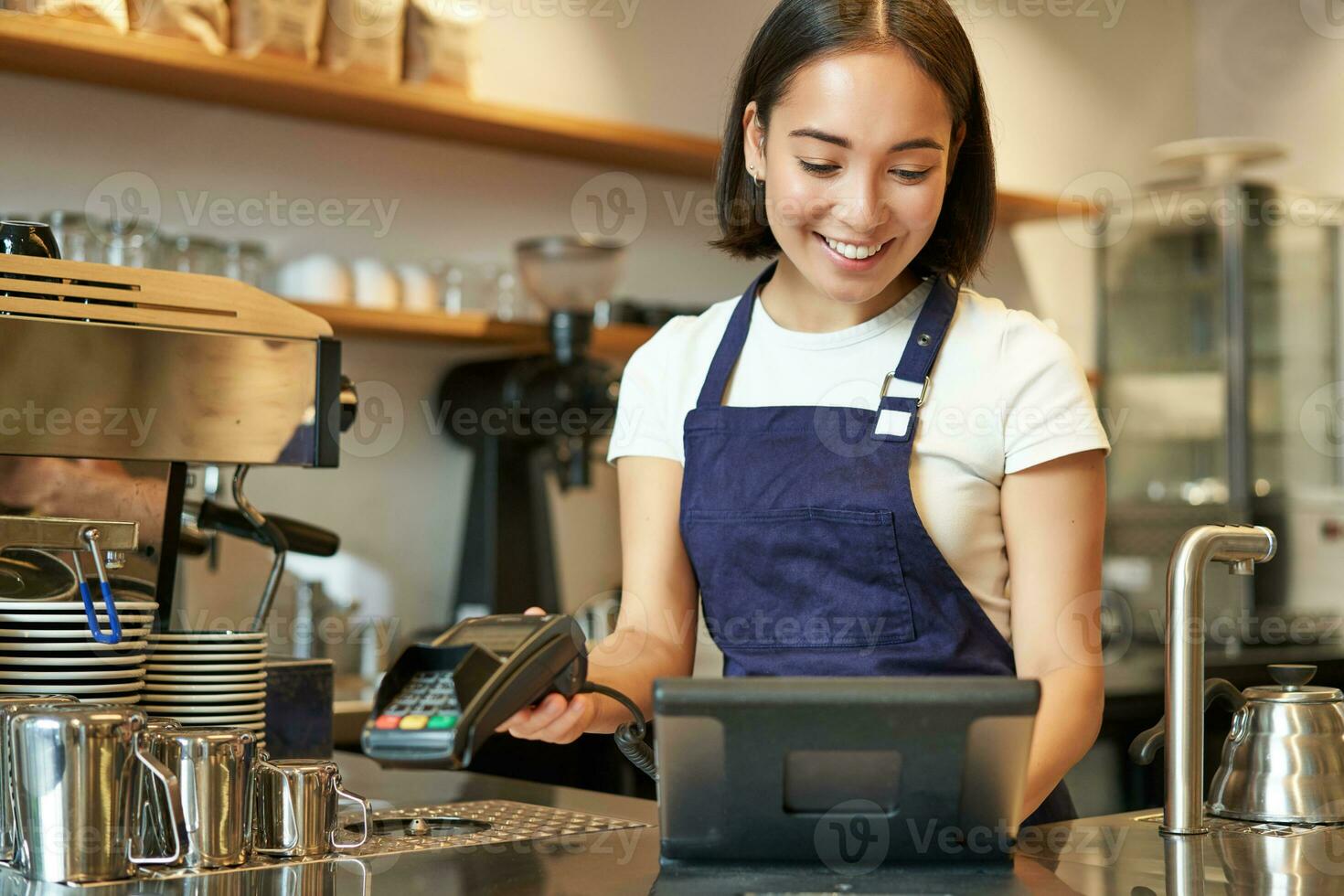 Smiling asian barista girl processing order, enter order in POS terminal, working at counter in coffee shop photo