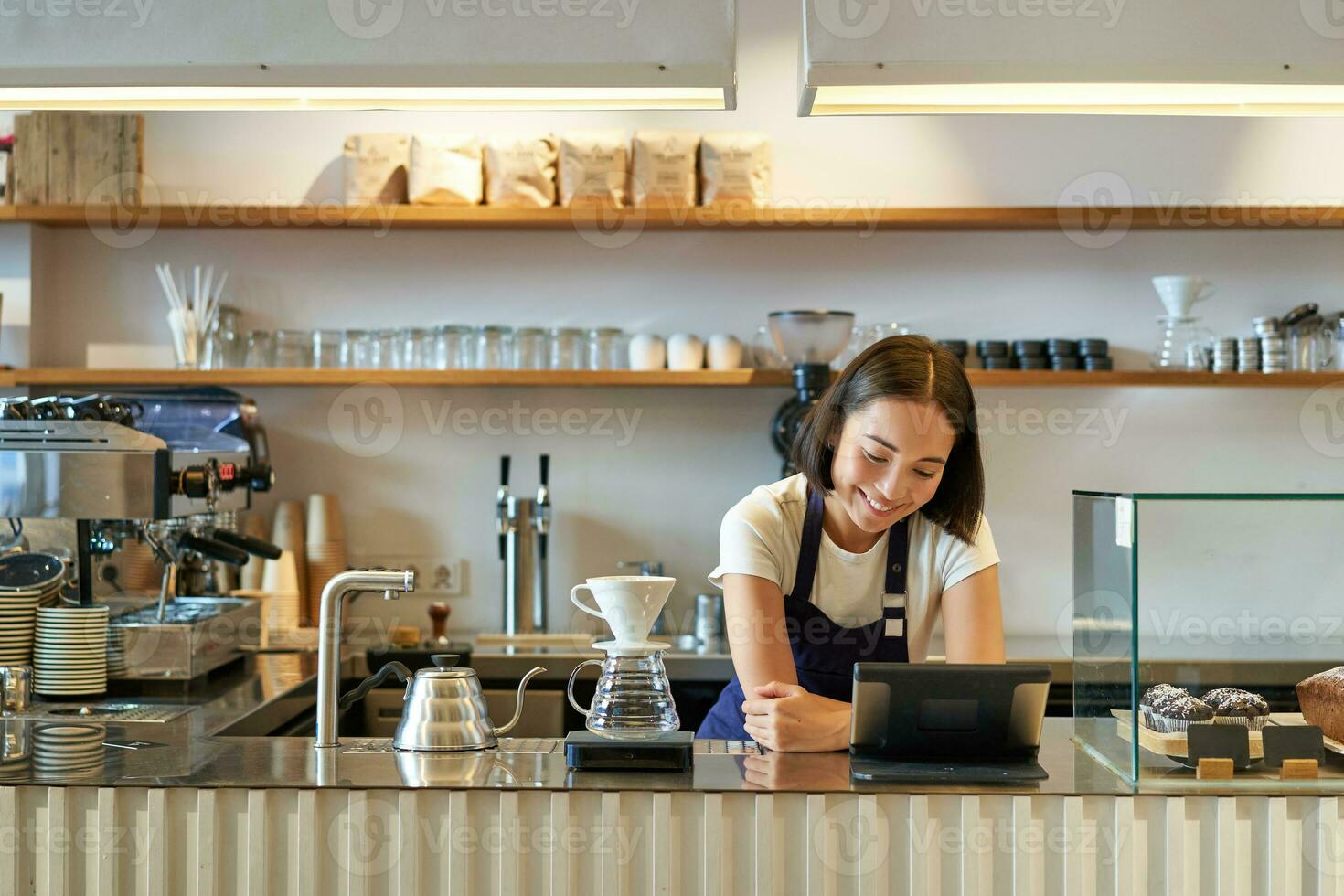 Happy smiling asian barista, girl behind counter, working with POS terminal and brewing filter kit, making coffee in cafe photo