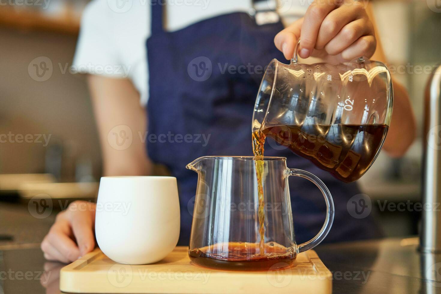 Close up of glass jar and a cup standing on cafe counter, barista pouring filter coffee and preparing order photo