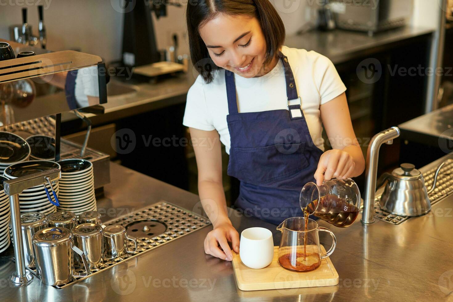 Barista in cafe pouring filter coffee, brewing and preparing order behind counter, wearing blue apron photo