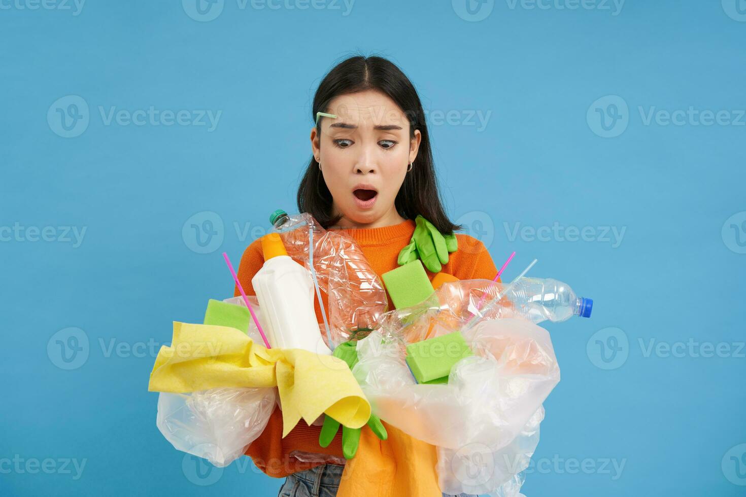 Shocked eco activist, collects loads of plastic to recycle, looking upset at bottles and unsorted garbage, blue background photo