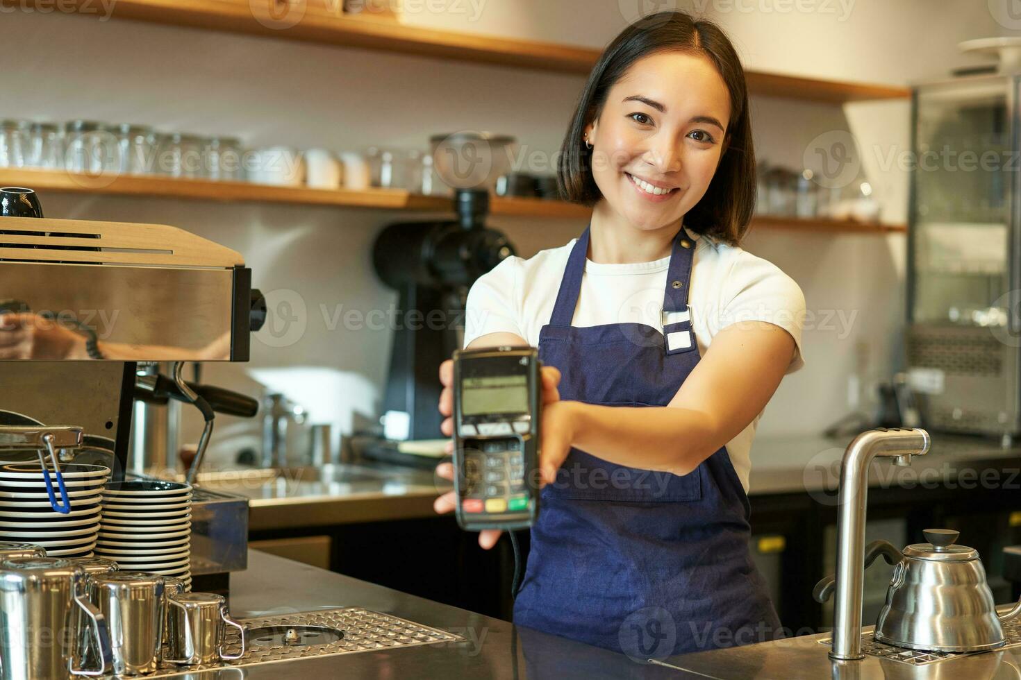 Smiling asian barista, coffee shop staff gives you credit card machine, processing payment with POS terminal, working in cafe photo