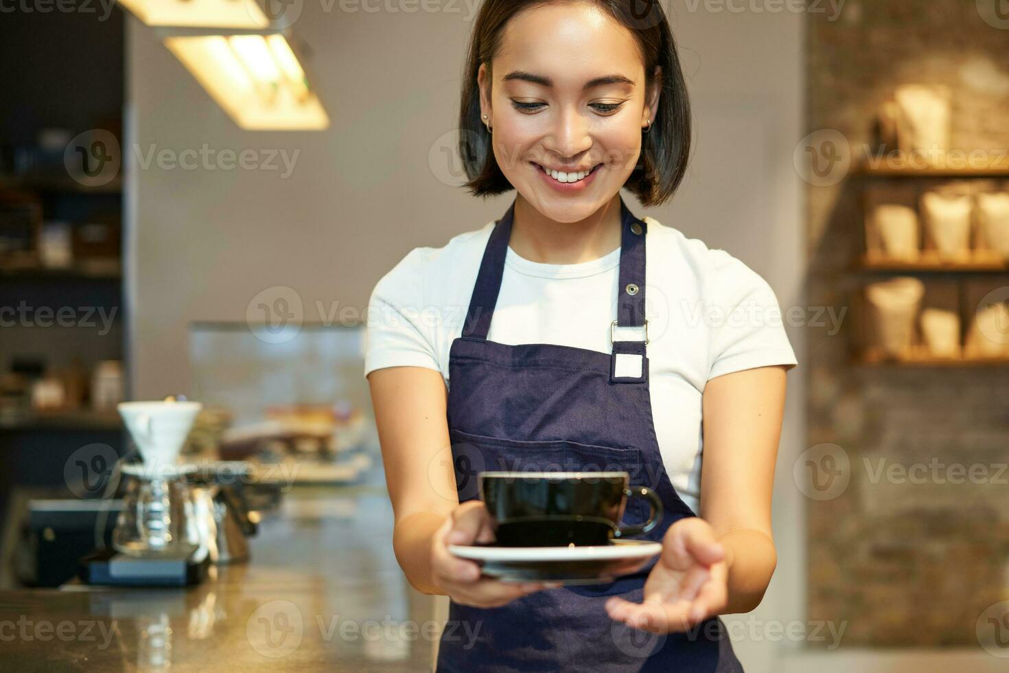 Smiling korean girl in uniform, working in cafe, giving you cup of coffee, preparing order for client photo