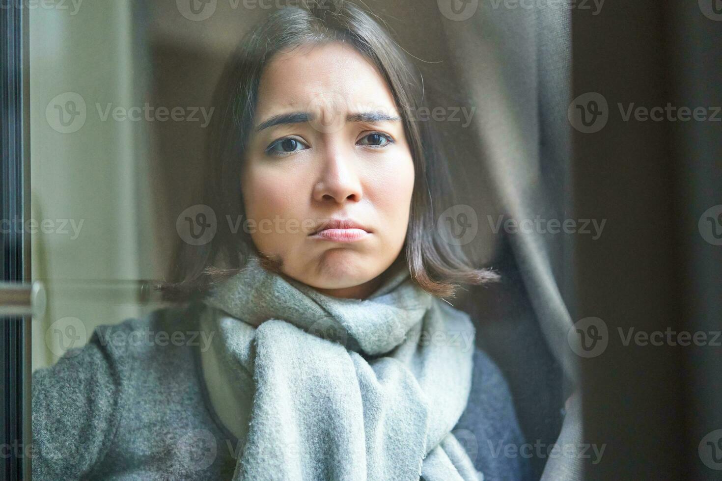 Portrait of sad ill woman staying at home, looking out of the window with jealous and upset face, cant leave home as being sick with covid-19 photo