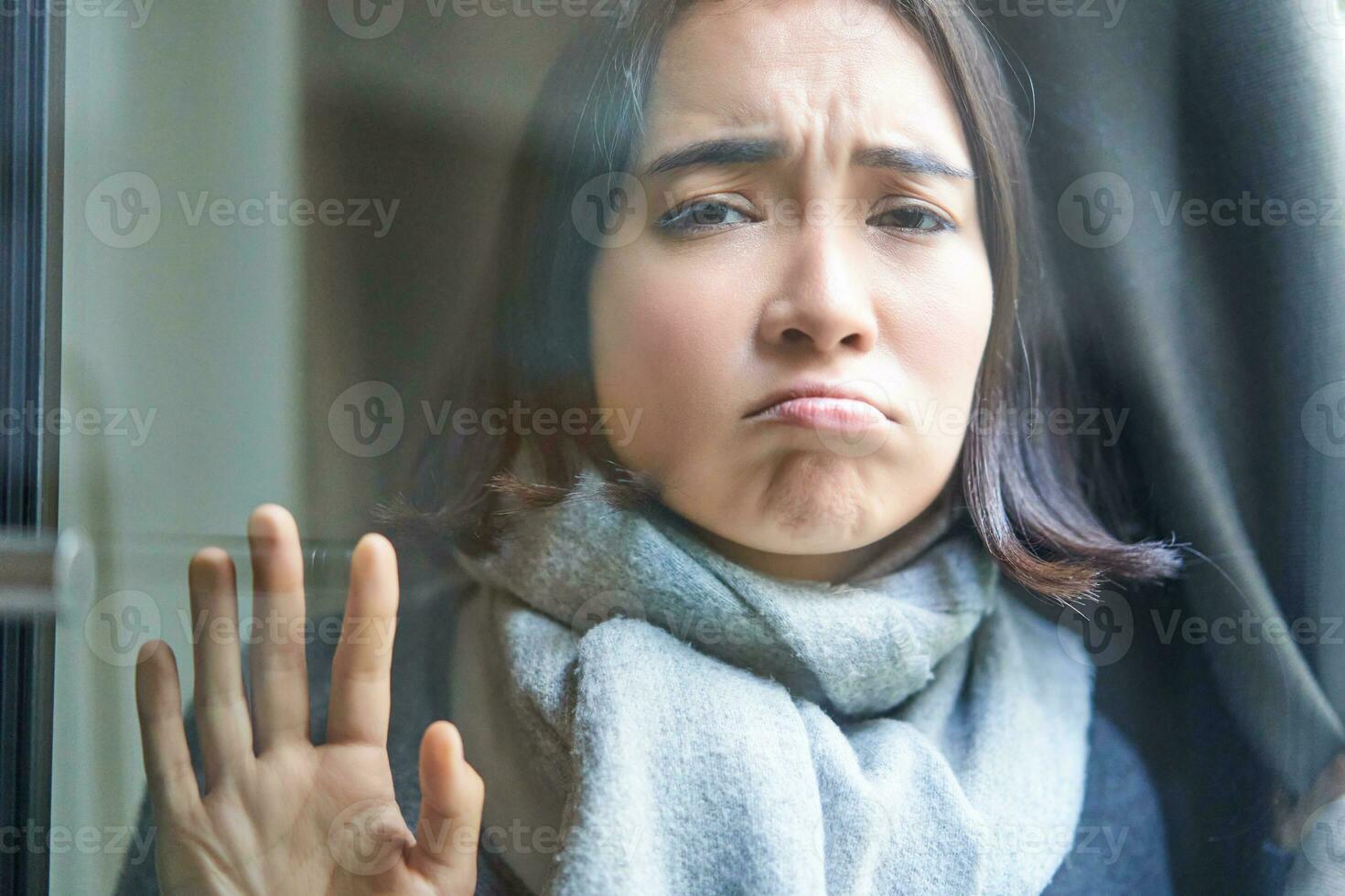 Portrait of sad ill woman staying at home, looking out of the window with jealous and upset face, cant leave home as being sick with covid-19 photo